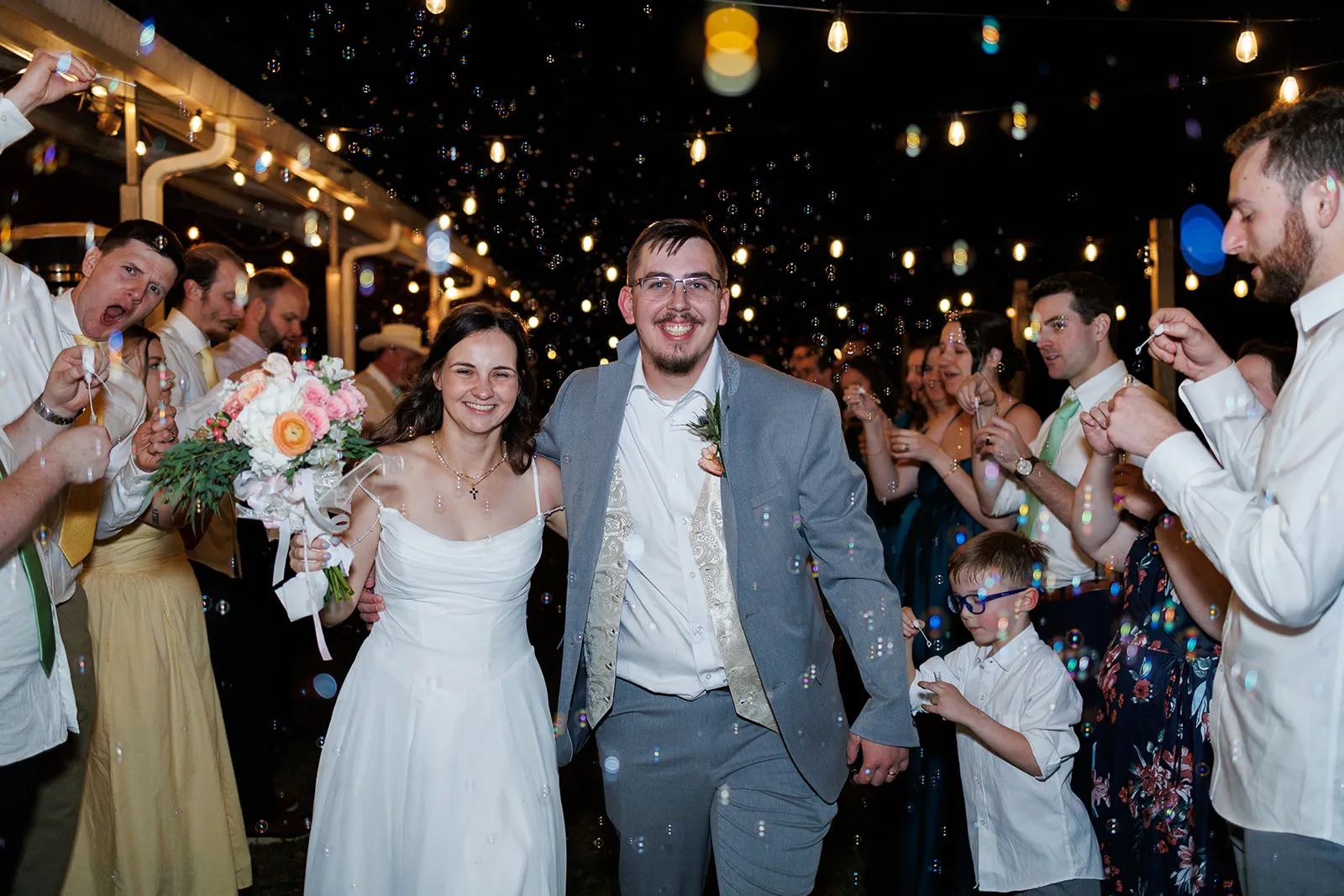 Couple walking through a nighttime bubble exit with guests gathered around them at The Heritage Barn